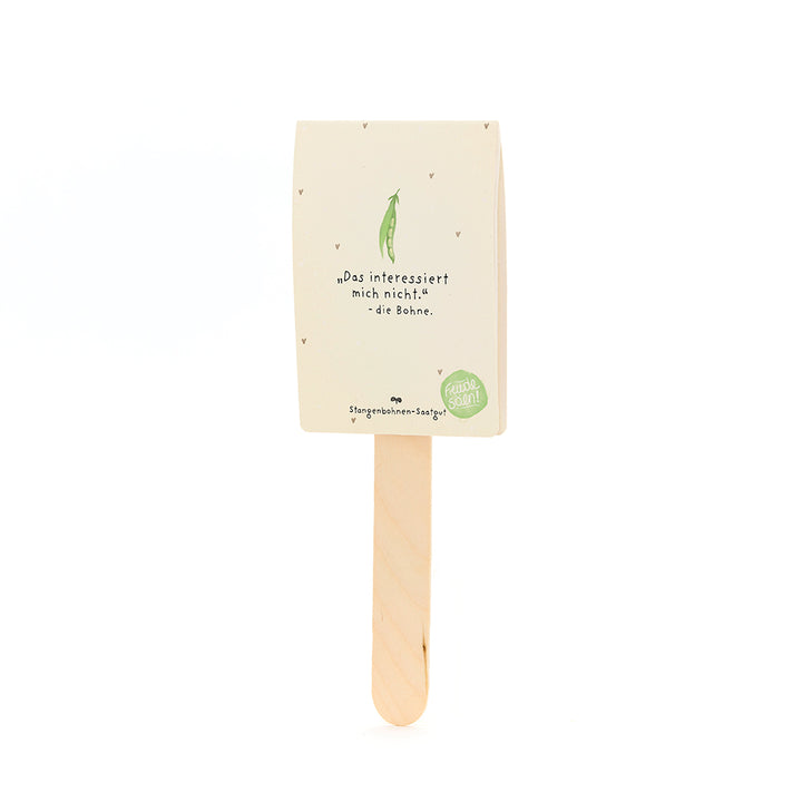Ein Stiel mit einer Verpackung darauf, beschriftet mit „Das interessiert mich nicht. – die Bohne“, darunter ein gezeichneter grüne Bohne, für Stangenbohnen-Saatgut.
