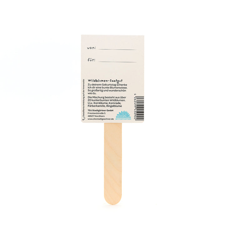Rückseite eines Wildblumen-Saatgut-Geschenks mit Holzstab, Feldern für "von" und "für", sowie Beschreibung der Blumensamenmischung auf Deutsch.