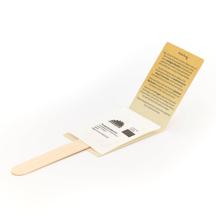 Holzstab mit angebrachtem Umschlag, der Samen enthält, sowie einer aufklappbaren Anleitung in deutscher Sprache.