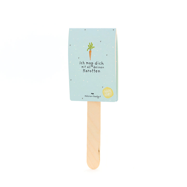 Ein Holzstäbchen mit hellblauem Schild, darauf eine Karottenzeichnung und der Text „Ich mag dich mit all deinen Karotten“.