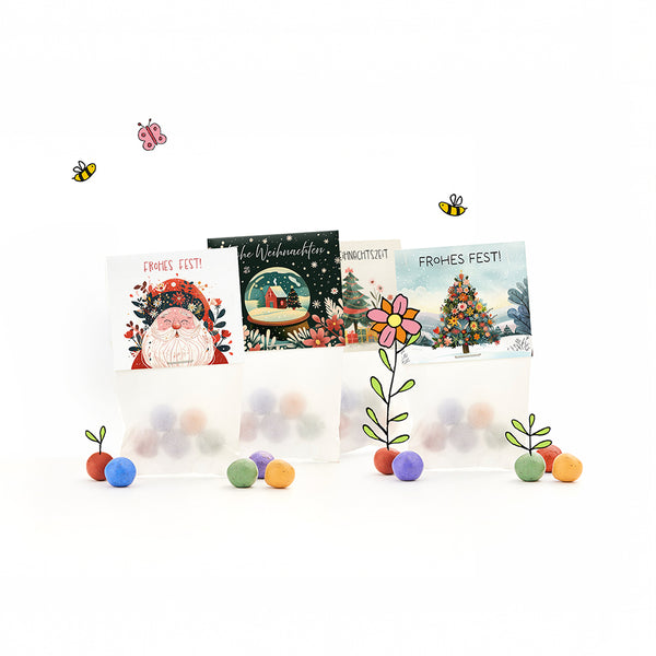 Drei weihnachtlich gestaltete Geschenktüten mit bunten Kugeln, illustrierten Weihnachtsmotiven und den Schriftzügen „Frohes Fest!“ sowie gezeichneten Blumen, Bienen und einem Schmetterling.