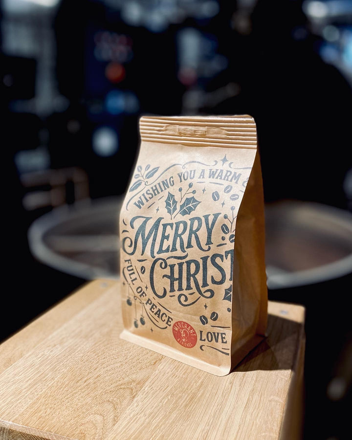 Papiertüte mit der Aufschrift "Merry Christmas" auf einem Holztisch, unscharfer Hintergrund.