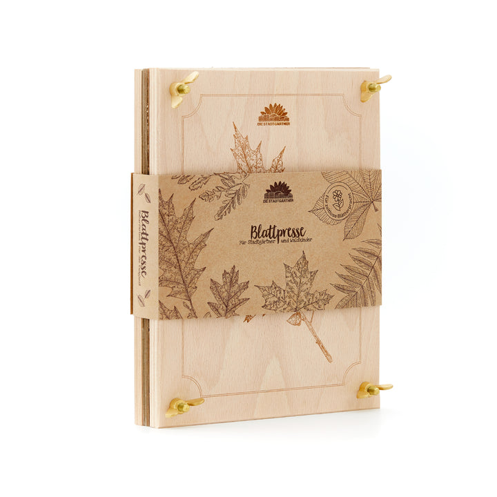 Holzpresse für Blätter mit botanischen Gravuren und braunem Papierband, darauf Blattmotive und der Schriftzug „Blattpresse“.