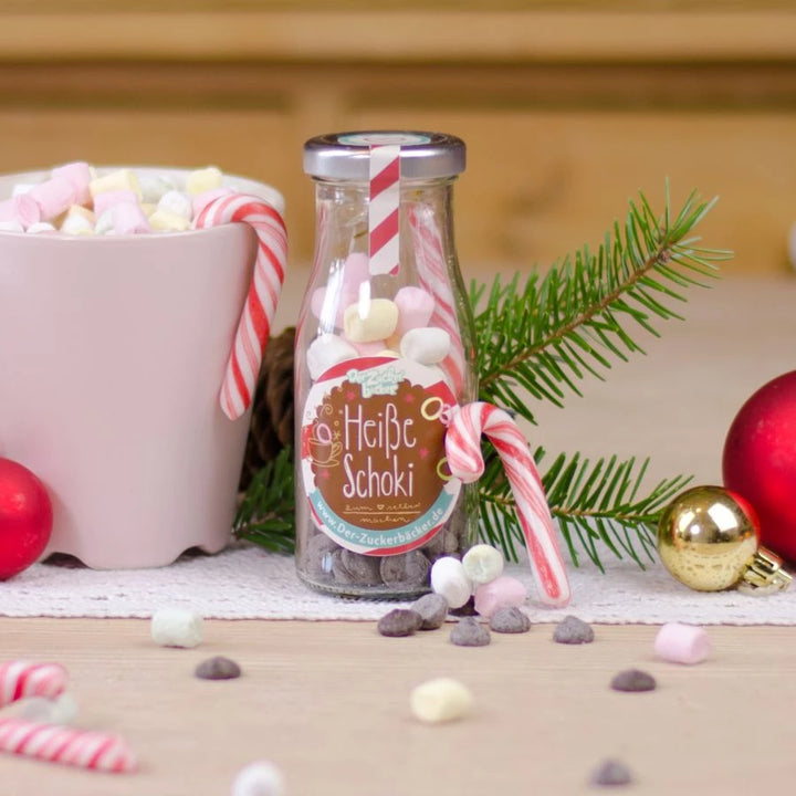 Flasche mit der Aufschrift "Heiße Schoki" neben Weihnachtsdeko und einer Tasse mit Marshmallows.
